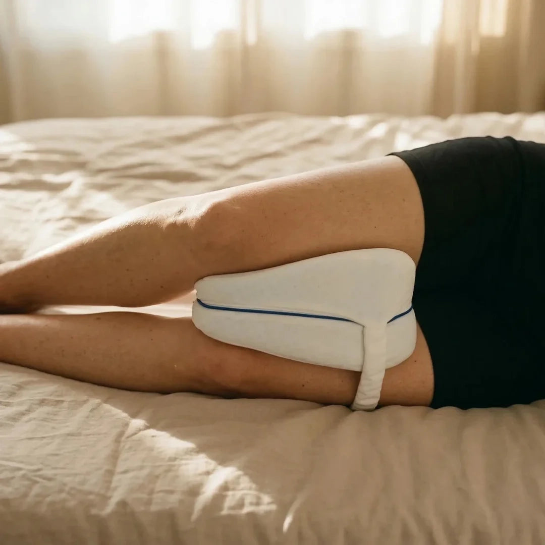 Femme dormant sur le côté avec un coussin de genou à mémoire de forme Velmi placé entre les genoux, dans une chambre à la lumière douce.